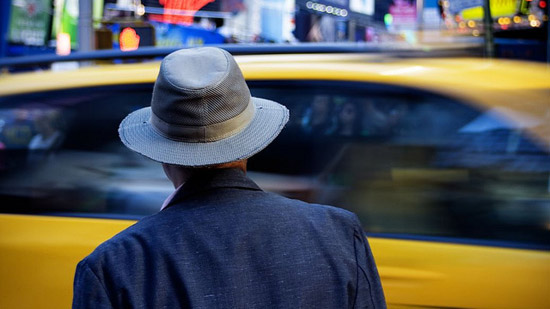 A man in a fedora looking at a taxi